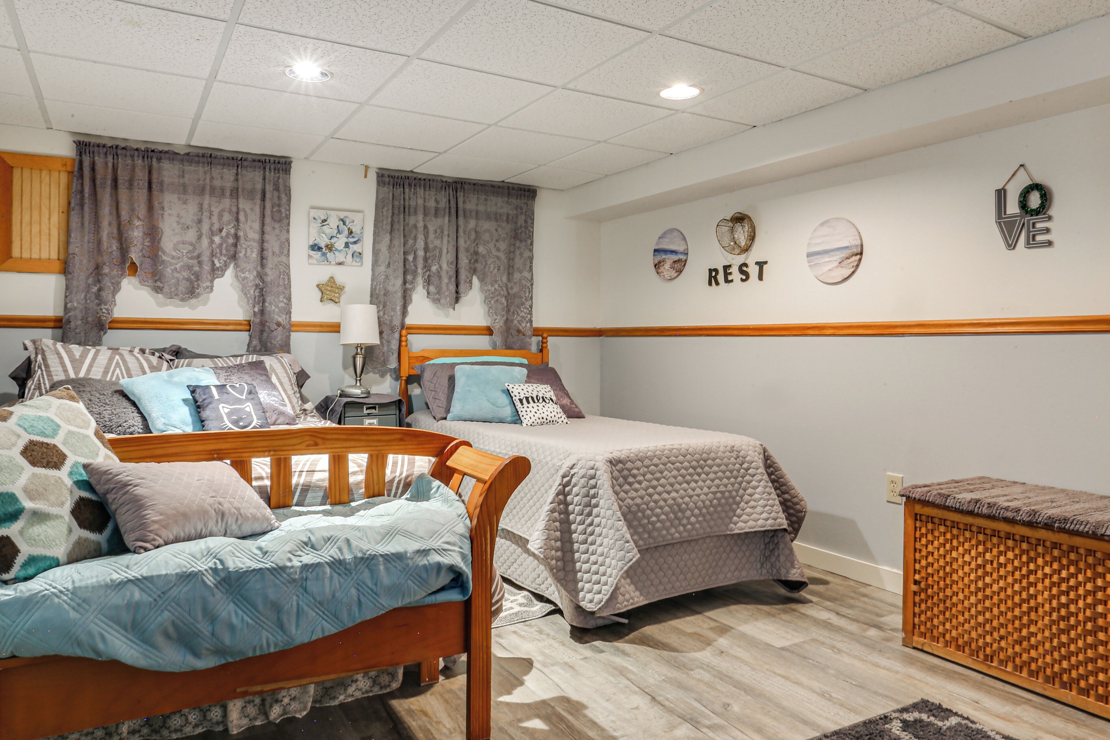 Une chambre avec deux lits, une tête de lit en bois, une table de chevet avec une lampe et un mur décoré de différents objets.