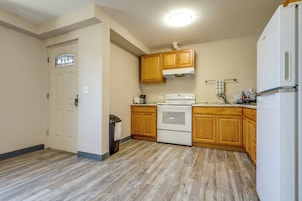 A kitchen with wooden cabinets, a white stove, and a trash can.