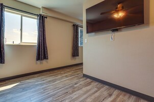 Una habitación con ventilador de techo, televisor de pantalla plana montado en la pared y ventana con cortinas.