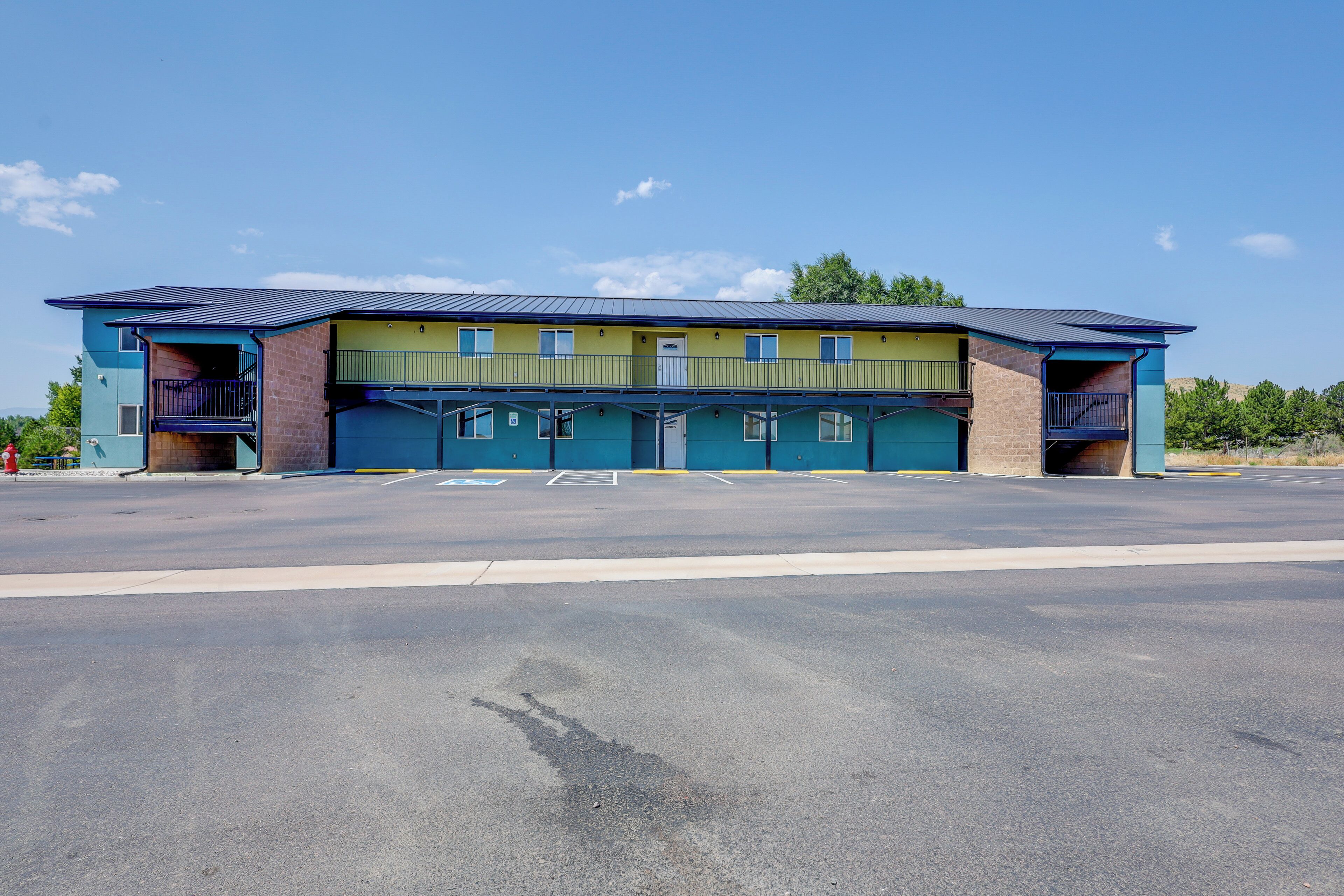 A two-story building with a flat roof, a parking lot in front, and a clear sky.