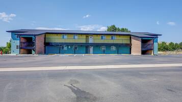 A two-story building with a flat roof, a parking lot in front, and a clear sky.