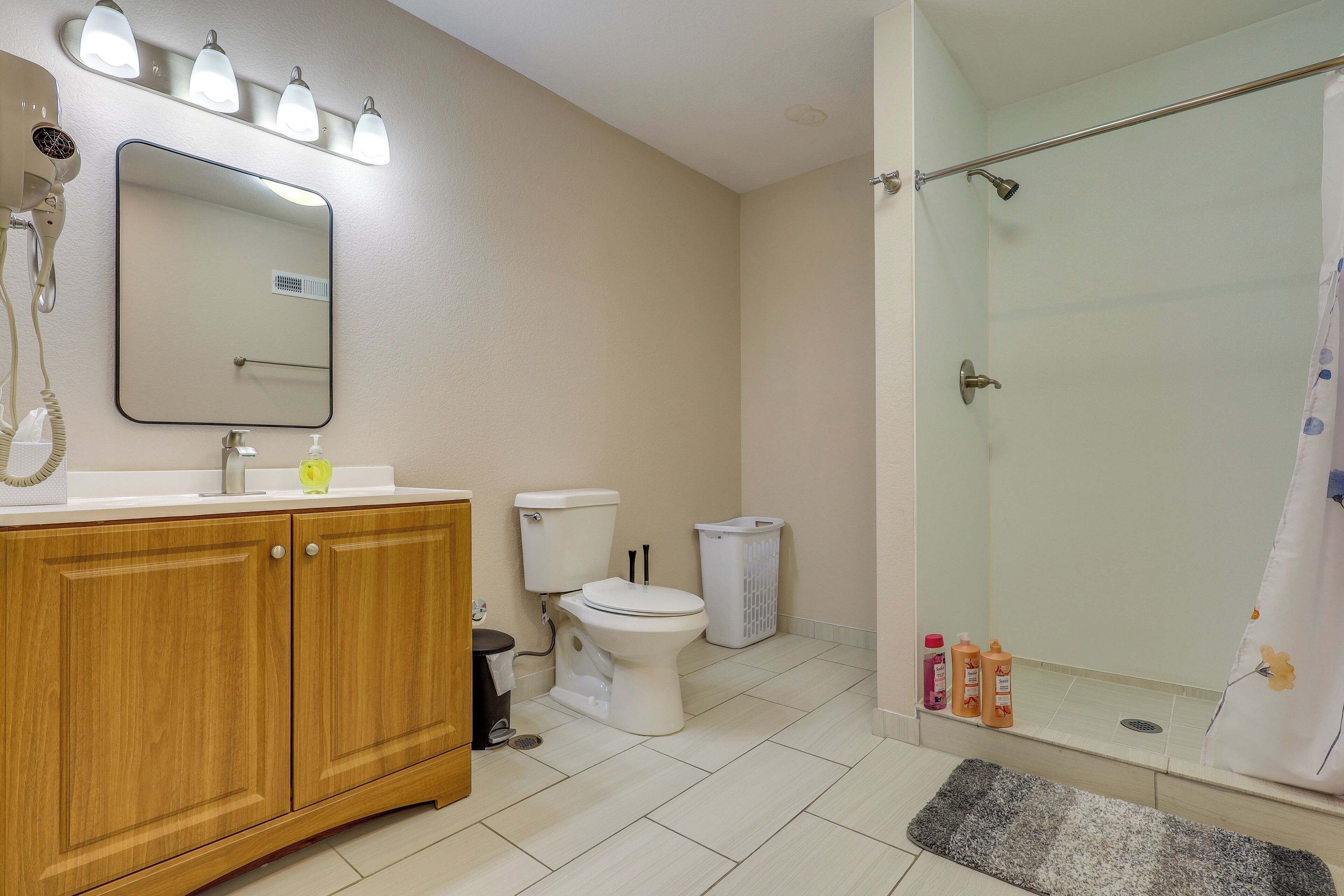 A bathroom with a wooden vanity, a toilet, a shower with a glass door, and a mirror with lights.