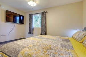 A bedroom with a bed, a television mounted on the wall, a window with curtains, and a ceiling fan.