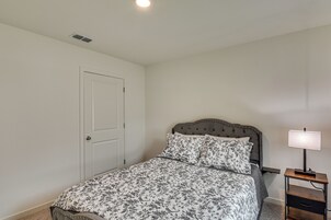 Un dormitorio con cama, una mesita de noche con lámpara, una puerta y una rejilla de ventilación en el techo.