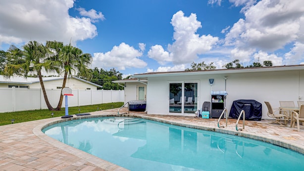 Uma piscina com deck revestido, hidromassagem coberta e área de estar com móveis de exterior.