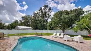 Uma piscina com escada de metal, rodeada por espreguiçadeiras brancas e um cercado branco.