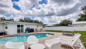 Piscina com espreguiçadeiras e uma mesa, cercada por um pátio de tijolos.