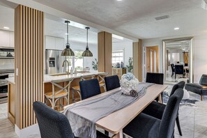 A modern dining area with a wooden table, black chairs, and pendant lighting. - Mid-term Stay in Sarasota! Home w/ Pool & Hot Tub (Sarasota)