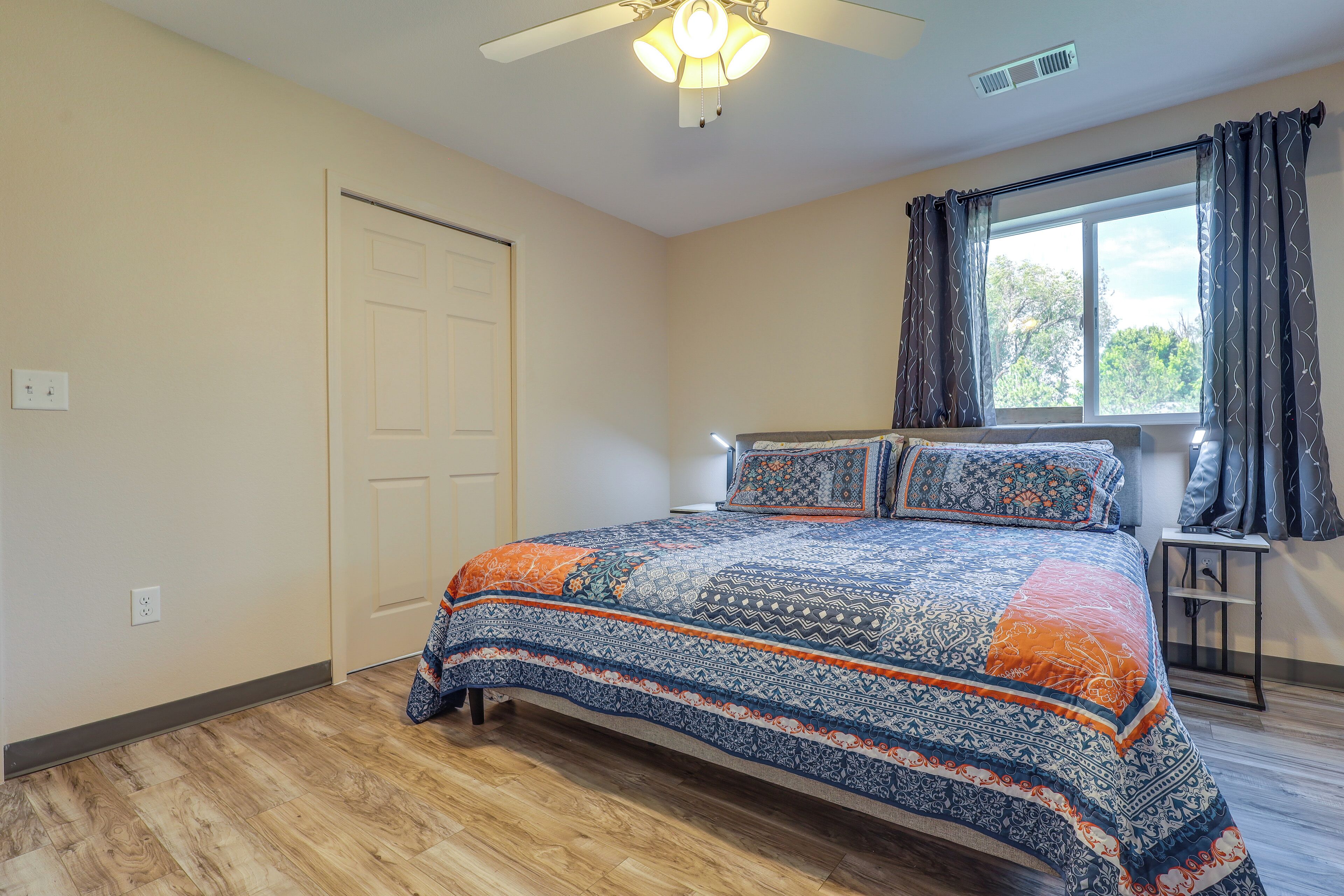 Un dormitorio con cama, ventana con cortinas, ventilador de techo y puerta.