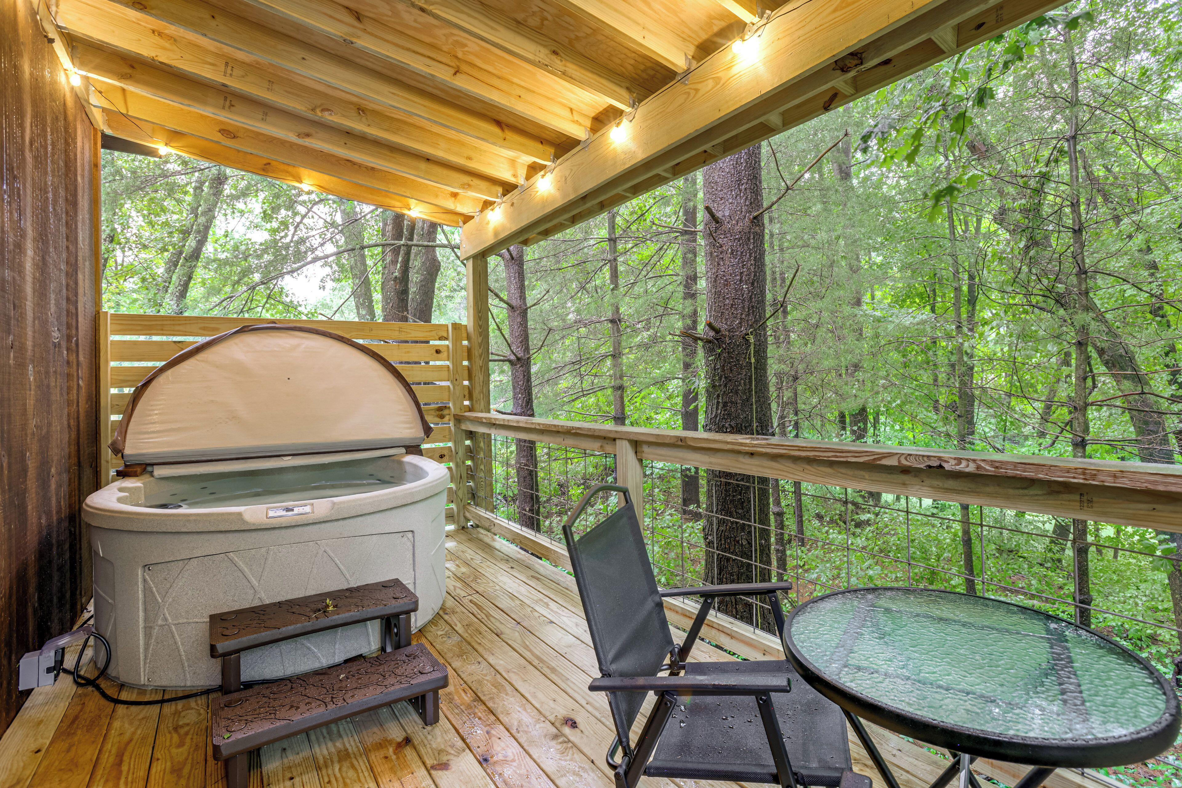 A wooden deck with a hot tub, a table, and a chair, overlooking a forest.