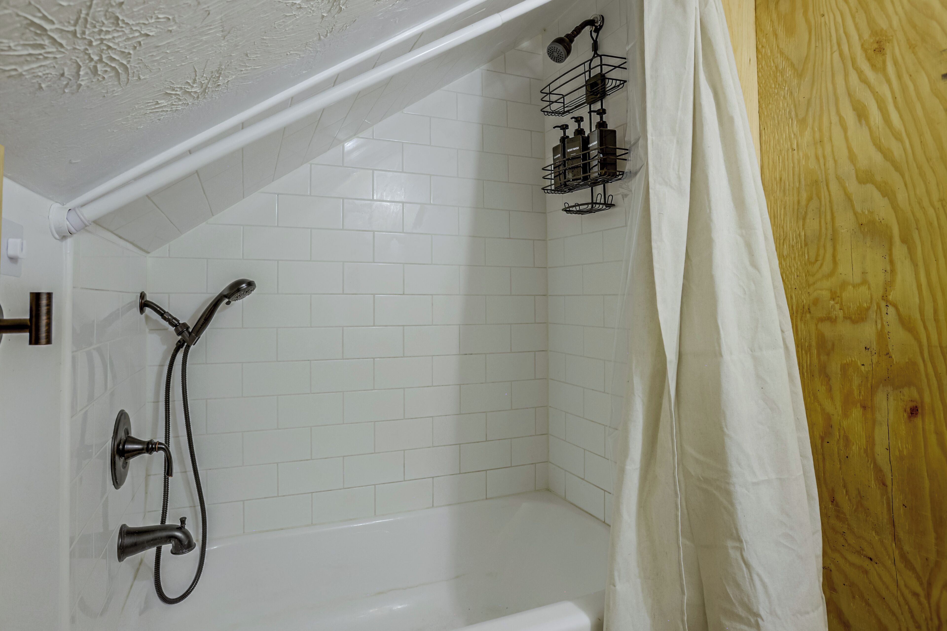 A bathroom with a shower, a bathtub, and a white tiled wall.