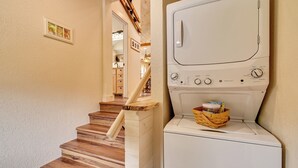 A laundry room with a white washer and dryer, wooden stairs, and a basket with laundry items. - Golf, Beaches, Slopes & More! Thompsonville Home (Thompsonville)
