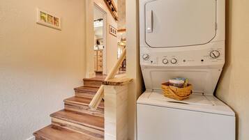 Une buanderie avec un lave-linge et un sèche-linge blancs, un escalier en bois et un panier rempli de linge.