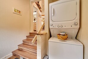 Ein Waschraum mit einer weißen Waschmaschine und einem Trockner, Holztreppen und einem Wäschekorb mit Wäsche.