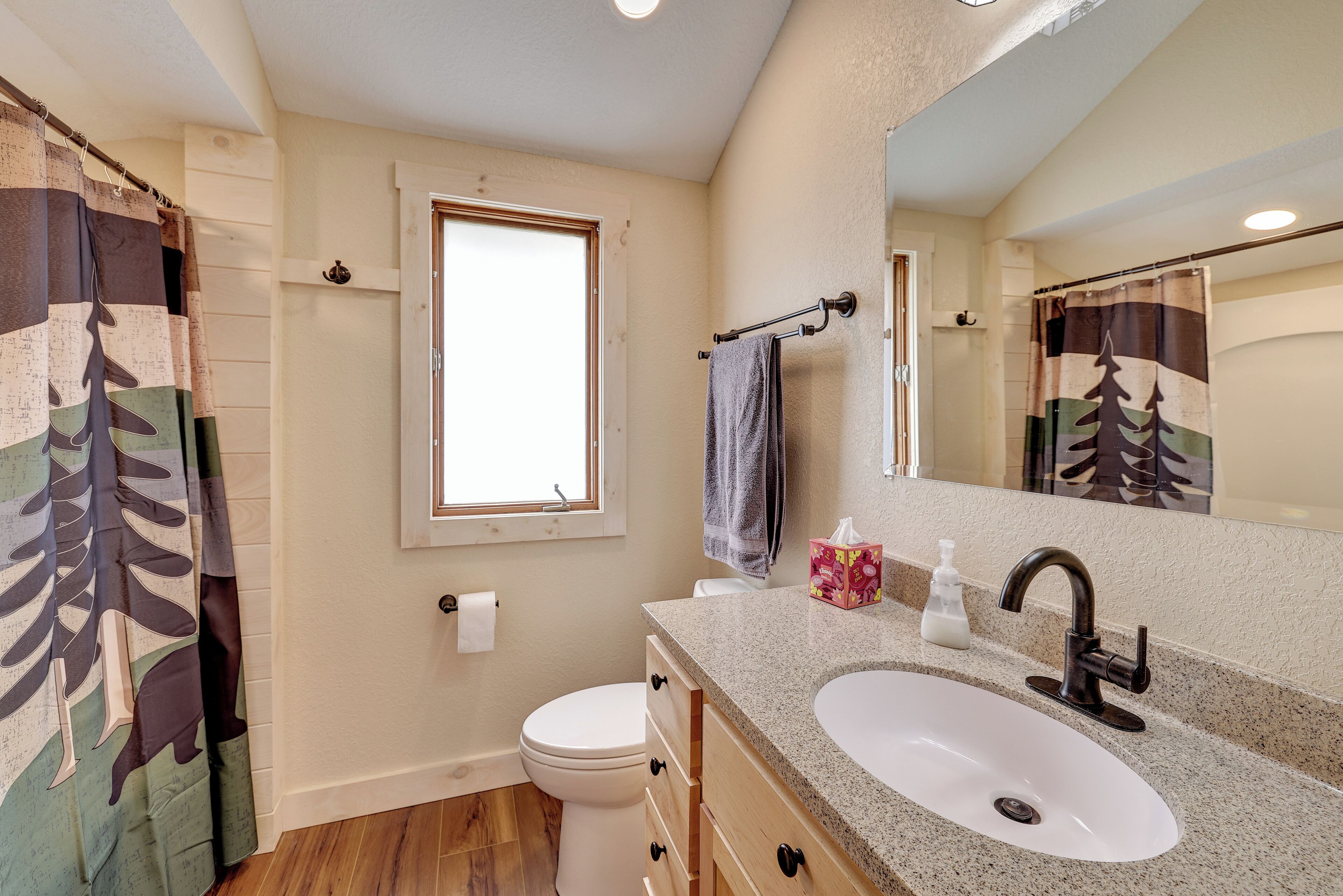 A bathroom with a toilet, sink, mirror, towel rack, and a window.
