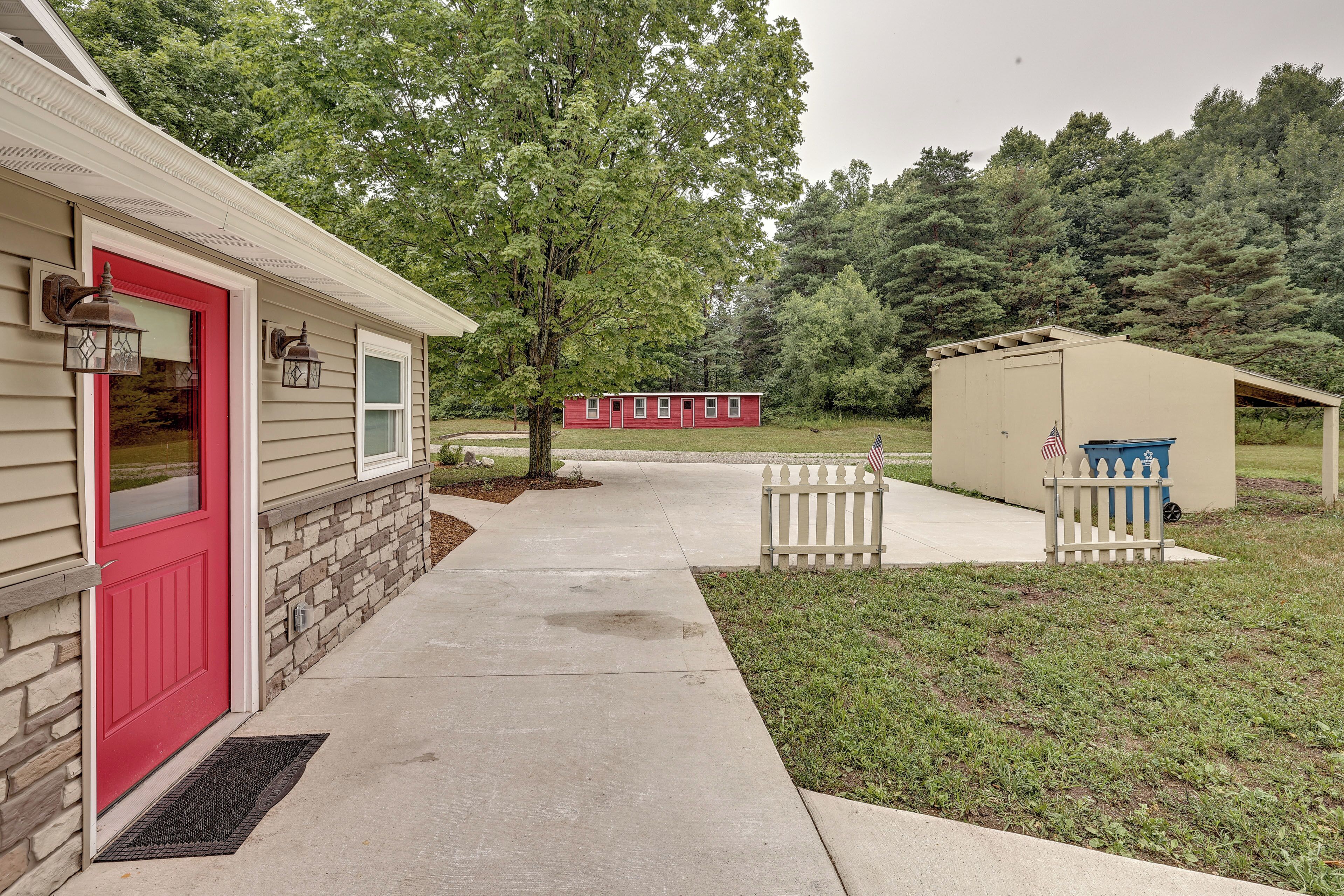 A residential property with a red door, a stone foundation, a concrete pathway, and a small shed with an American flag.