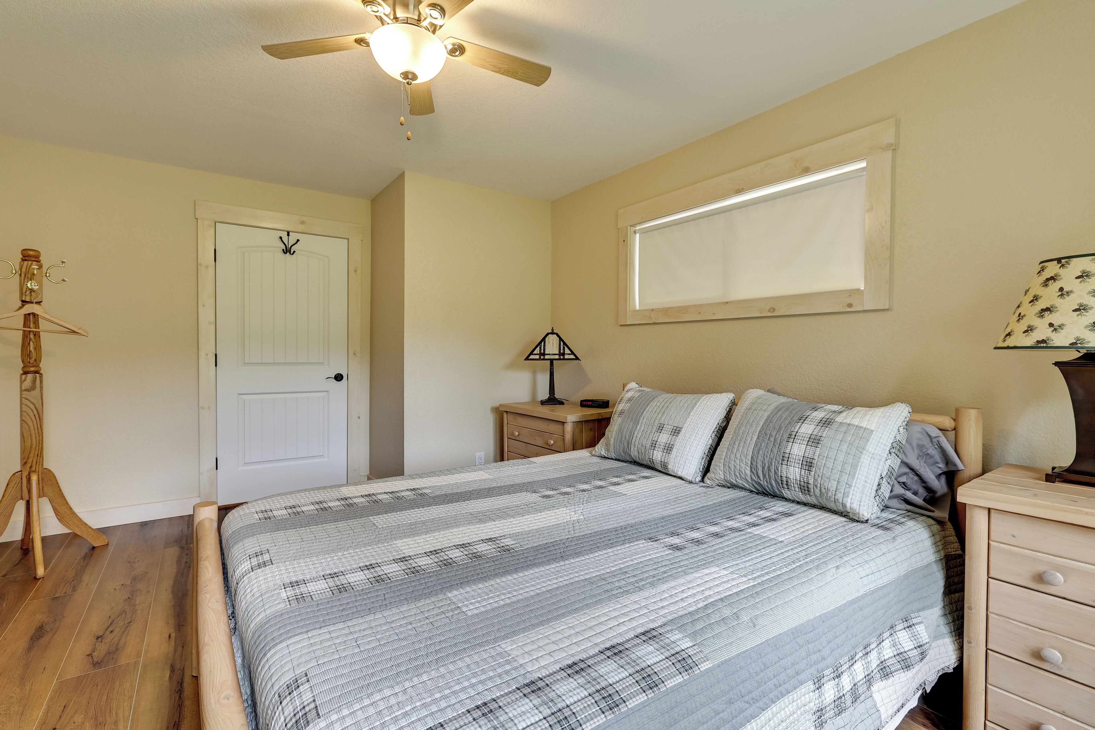 A bedroom with a bed, a ceiling fan, a nightstand, a lamp, a window, and a door.