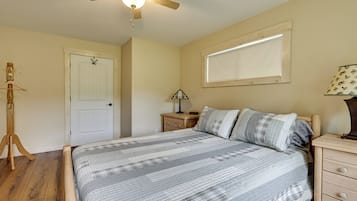 Een slaapkamer met een bed, een plafondventilator, een nachtkastje, een lamp, een raam en een deur.