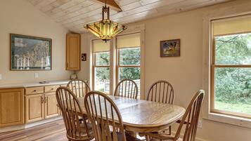 Un espace repas comprenant une table et des chaises en bois, un luminaire suspendu et une grande fenêtre donnant sur un paysage verdoyant.