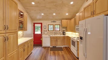 A kitchen with wooden cabinets, a red door, a white refrigerator, and a stove.