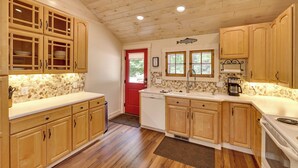 A kitchen with wooden cabinets, a red door, and a stone backsplash. - Golf, Beaches, Slopes & More! Thompsonville Home (Thompsonville)