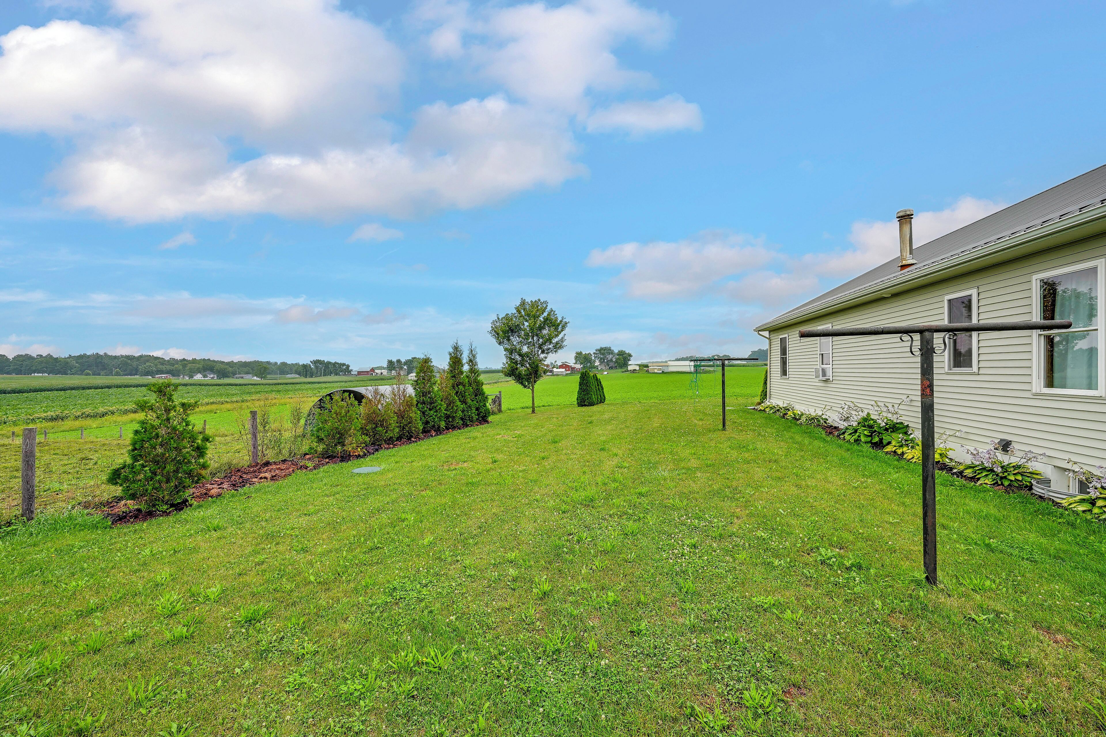 A grassy yard with a house, a metal fence, and a clear sky.