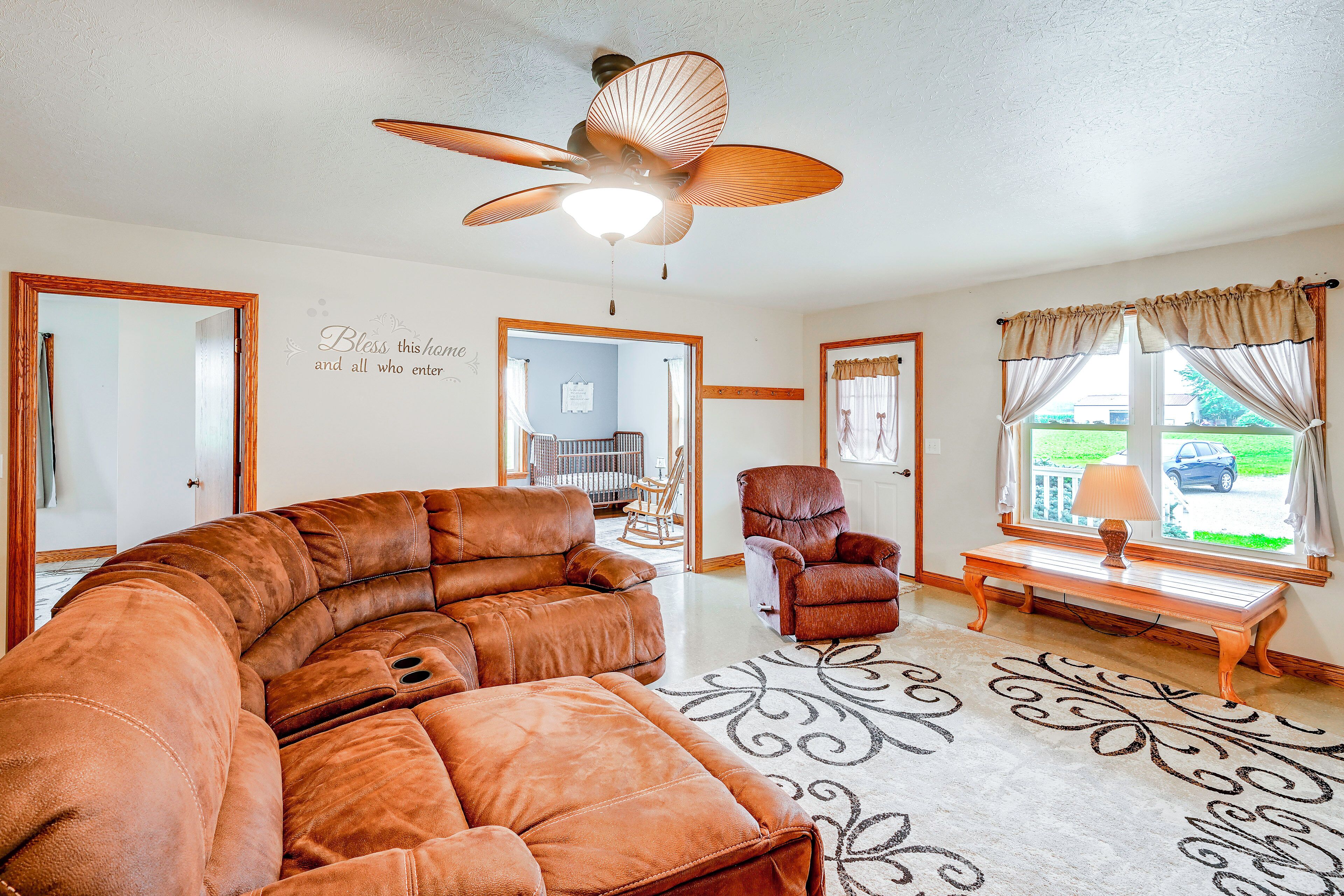 A living room with a brown leather sectional sofa, a rocking chair, a wooden bench, and a ceiling fan.