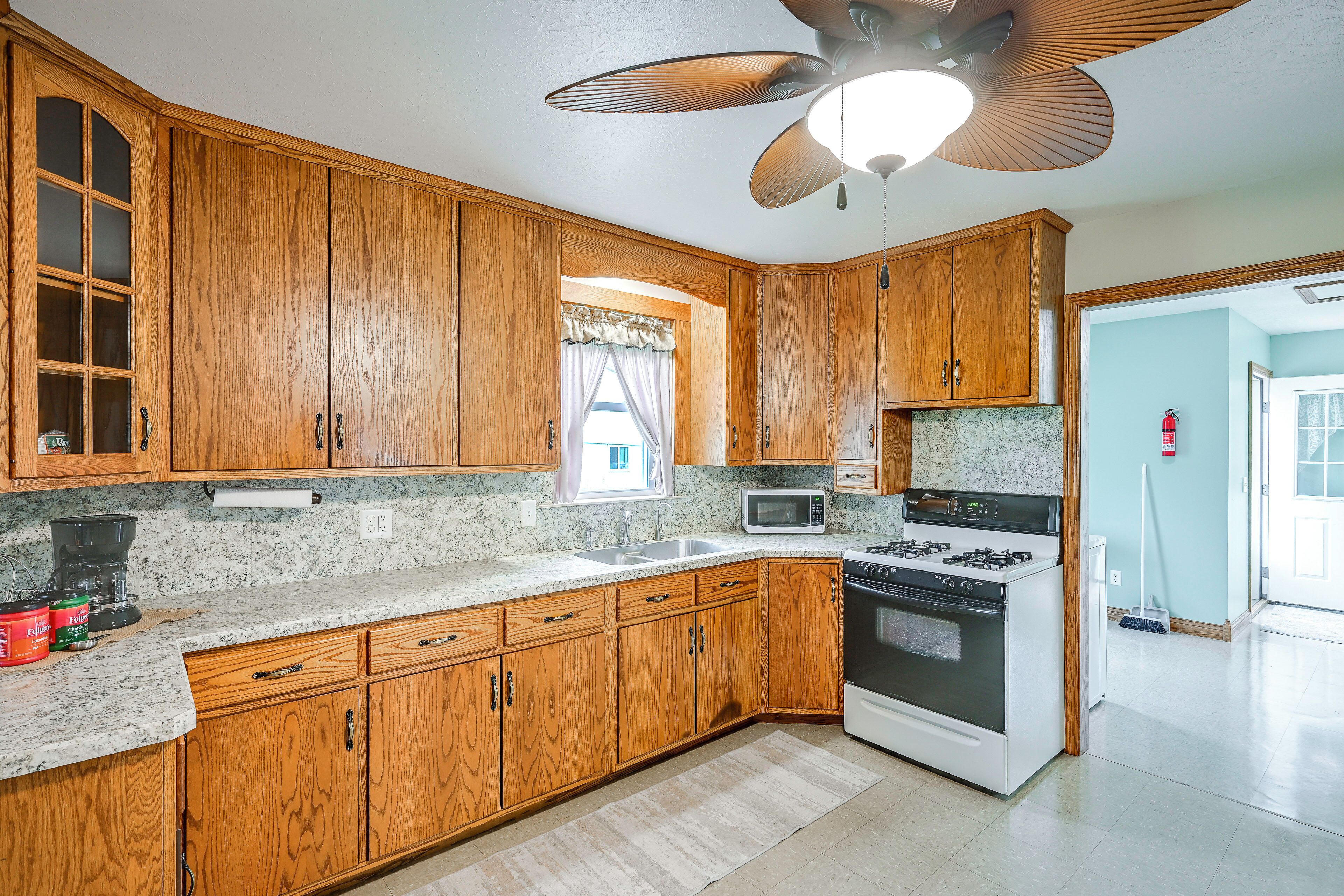 A kitchen with wooden cabinets, a microwave, stove, and a ceiling fan.