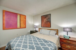 A bedroom with a bed, two bedside tables, a nightstand, a large abstract painting, and a smaller framed artwork on the wall.