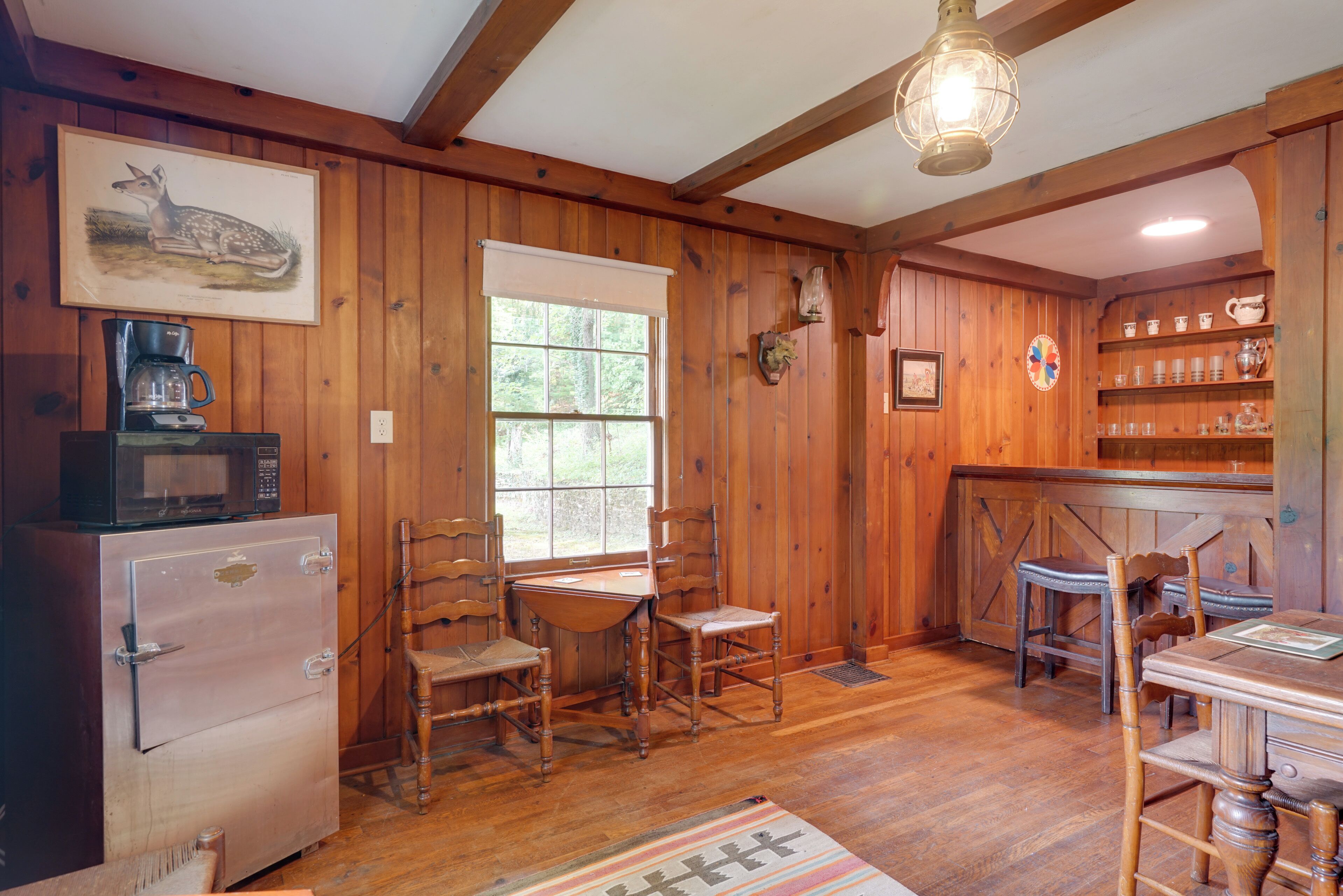 A wooden interior with a refrigerator, microwave, dining table, chairs, and a kitchen area with shelves.