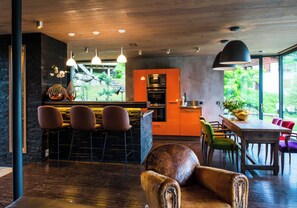 A modern kitchen with a bar area, wooden flooring, and a view of greenery outside. - Contemporary chalet with exceptional views, nestled in a natural setting (Praz-sur-Arly)