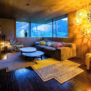 A modern living room with a sofa, a round table, and a view of a forest through large windows. - Contemporary chalet with exceptional views, nestled in a natural setting (Praz-sur-Arly)