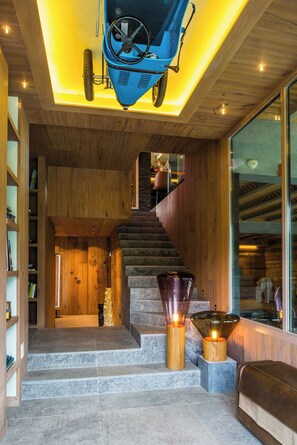 A modern interior with a staircase, wooden walls, and a blue vehicle suspended from the ceiling. - Contemporary chalet with exceptional views, nestled in a natural setting (Praz-sur-Arly)