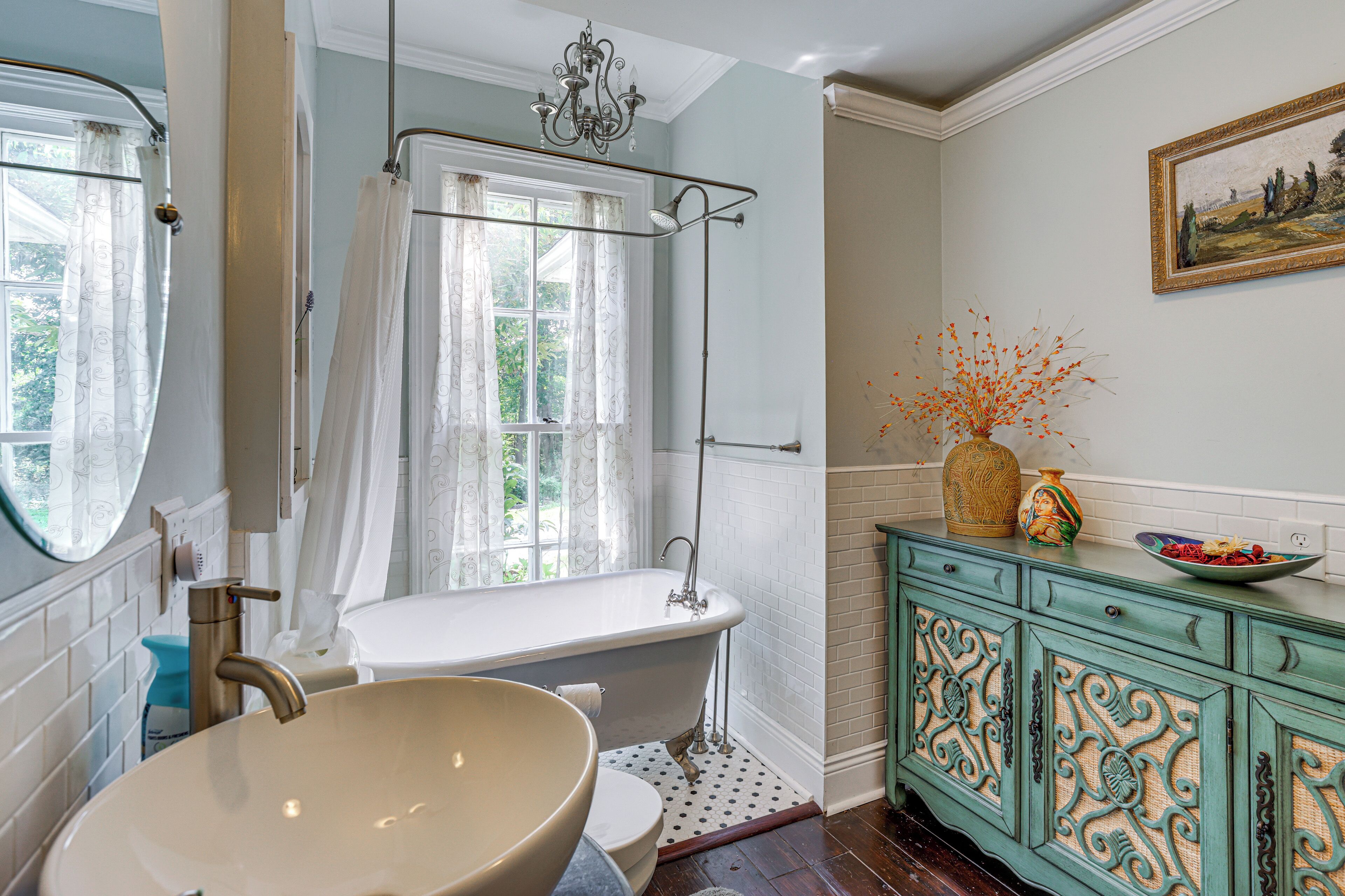 A bathroom with a freestanding bathtub, a large basin sink, a vanity with decorative cabinet doors, and a window with curtains.