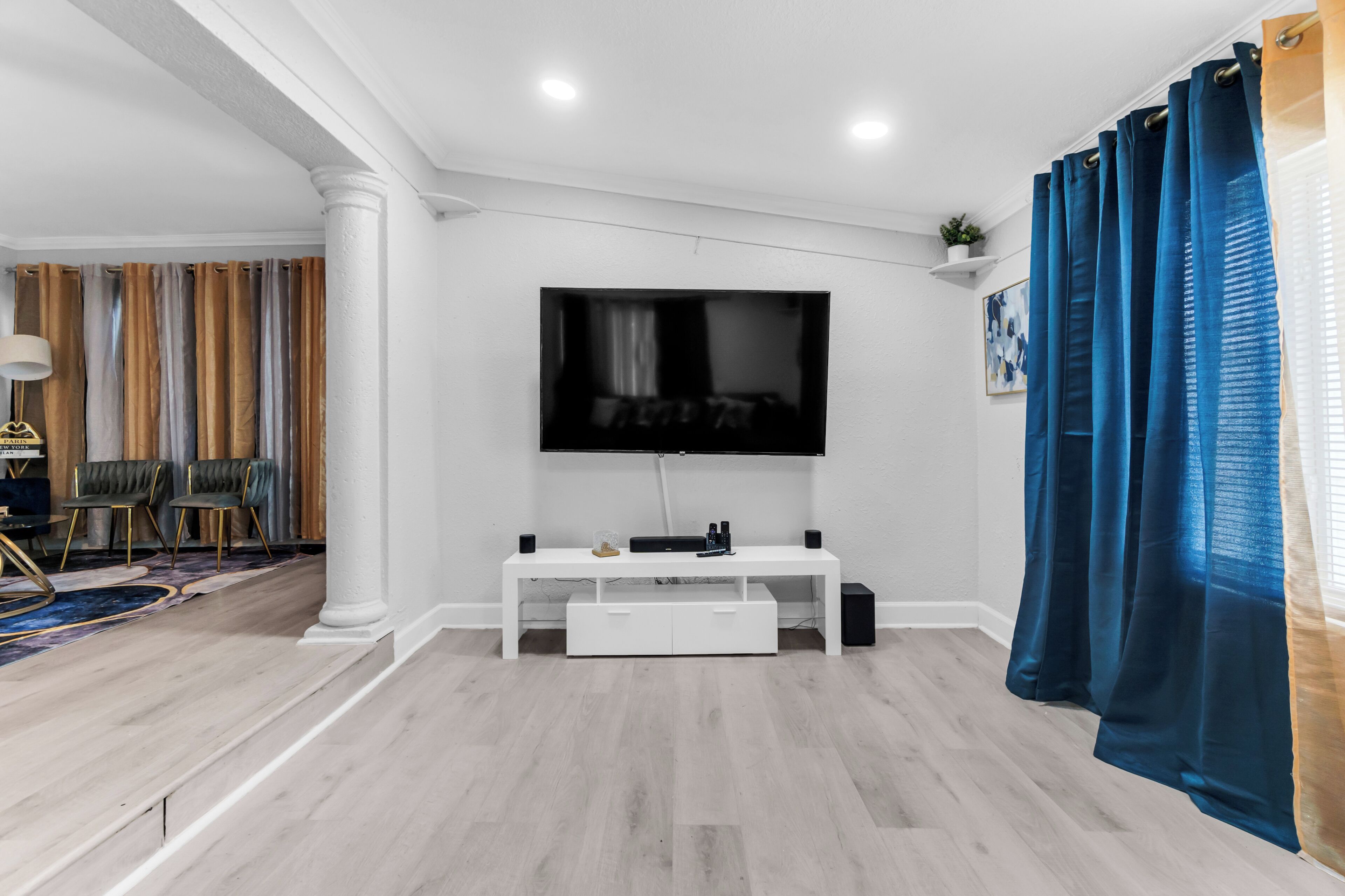 Un salon avec un téléviseur à écran plat fixé au mur, un meuble de rangement blanc et un rideau bleu.