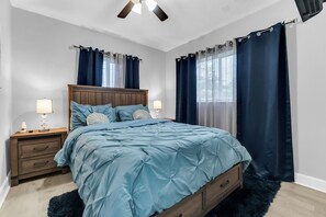 A bedroom with a wooden headboard, a bed with blue bedding, two bedside tables with lamps, and a ceiling fan. - Awesome 3-bedroom house in enchanting Miami Gardens with AC (Miami gardens)