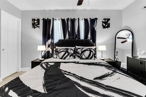 Une chambre à coucher avec un lit, deux lampes de chevet, un miroir et un ventilateur de plafond.