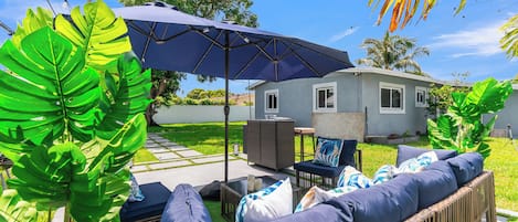 A patio area with outdoor furniture, a large umbrella, and lush greenery.