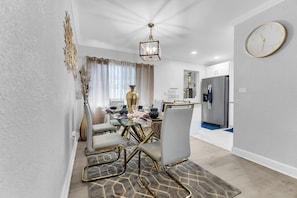 A modern dining area with a glass table, gold chairs, and a chandelier. - Awesome 3-bedroom house in enchanting Miami Gardens with AC (Miami gardens)