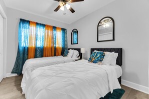 A hotel room with two beds, a ceiling fan, a window with sheer curtains, and a mirror on the wall. - Awesome 3-bedroom house in enchanting Miami Gardens with AC (Miami gardens)