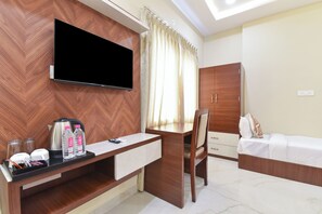 A hotel room with a flat-screen TV, wooden furniture, a desk, a chair, a bed, and a wardrobe. - Hotel Gold Coin (Jaipur)