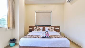 Una habitación de hotel con cama, ventana con cortinas, aire acondicionado de pared y luz en el techo.