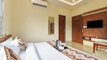 A hotel room with a bed, bedside table, air conditioning unit, television, and a mirror.