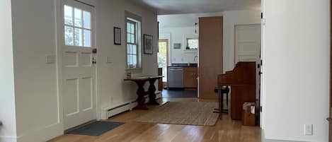 Um corredor espaçoso com piso de madeira, uma sala de jantar com mesa e cadeiras, e uma cozinha com armários e pia.