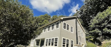 A two-story house with a front porch and multiple windows, surrounded by trees and a clear sky.