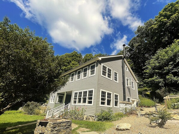 A two-story house with a front porch and multiple windows, surrounded by trees and a clear sky.