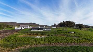 Una casa moderna con un amplio jardín delantero, un estanque y un paisaje montañoso al fondo.