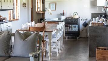 A dining area with a wooden table and chairs, a kitchen with a stove and cabinets, and a sofa with cushions.