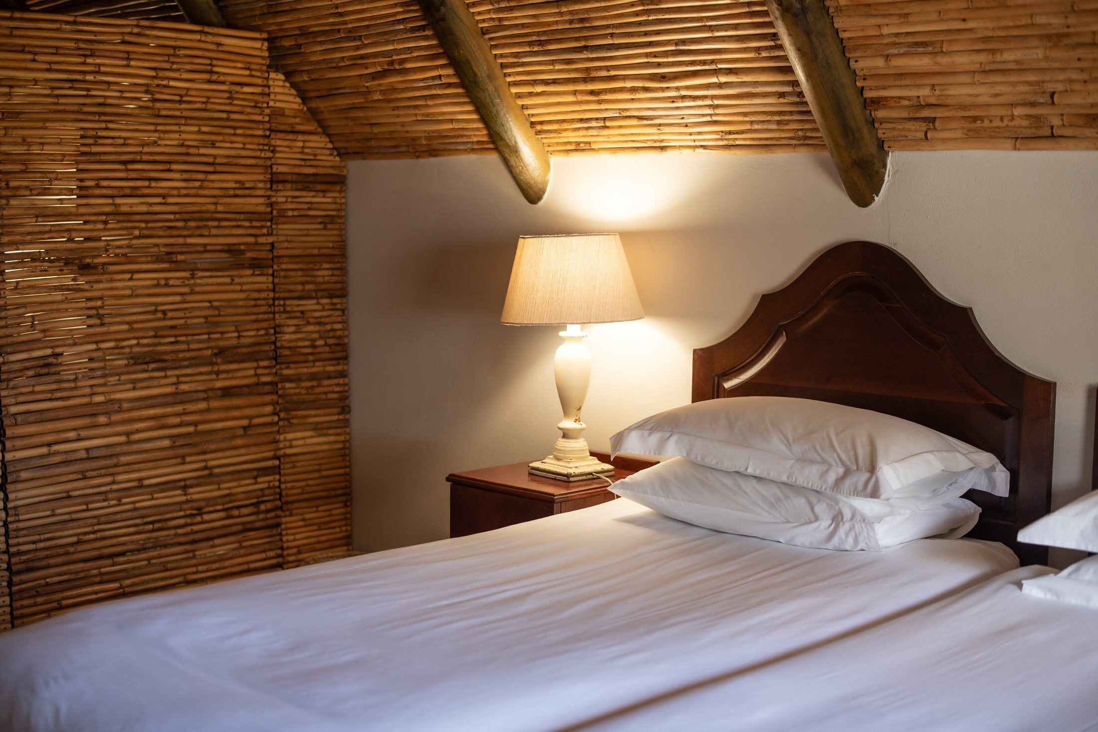 Een hotelkamer met een bed, nachtkastje, lamp en houten plafond.