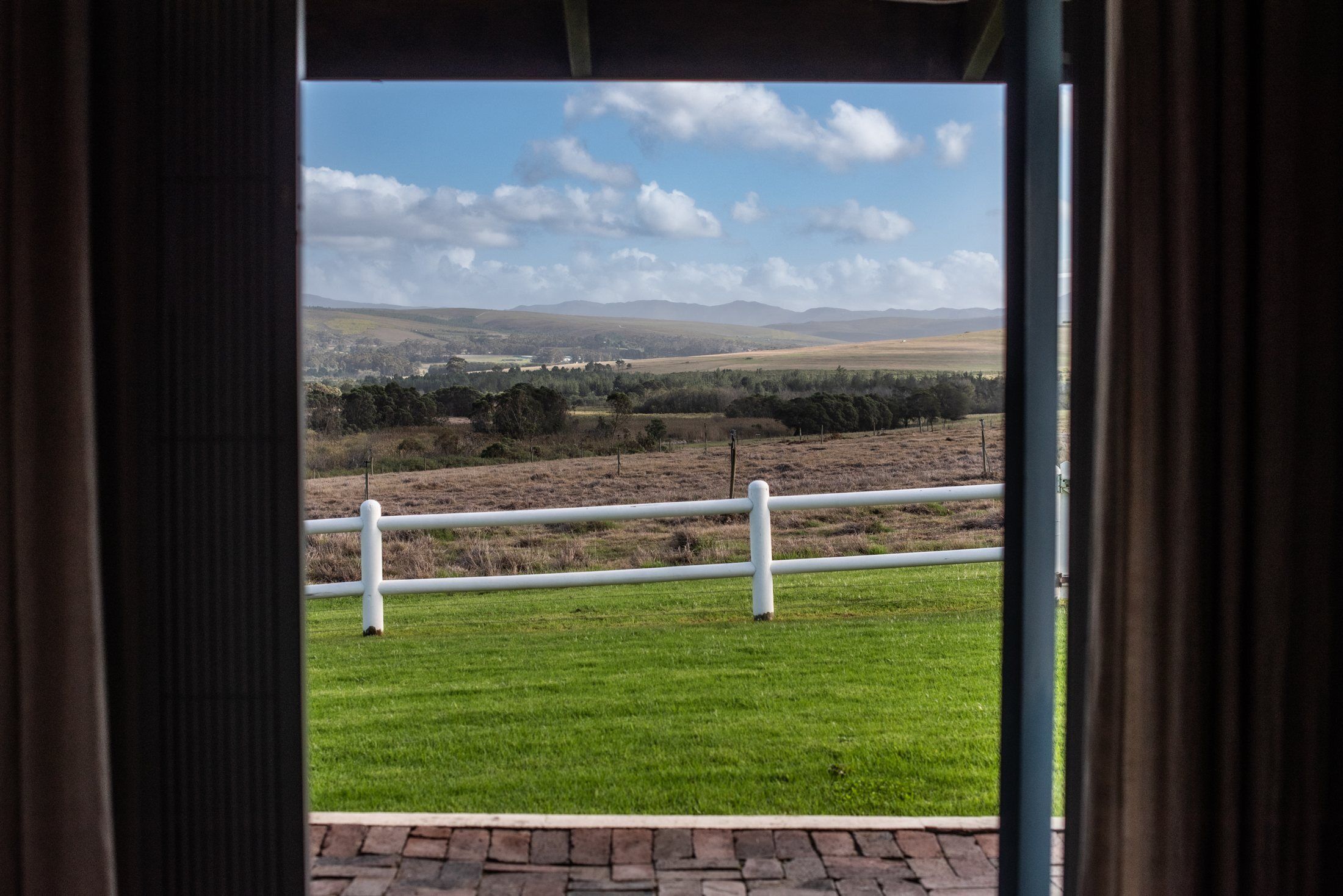 A view through a window with a white railing, a grassy area, and distant hills.